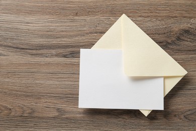 Photo of Blank invitation card and envelope on wooden table, top view. Space for design