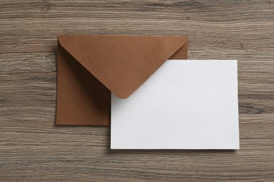 Photo of Blank invitation card and envelope on wooden table, top view. Space for design