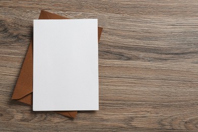 Photo of Blank invitation card and envelope on wooden table, top view. Space for design