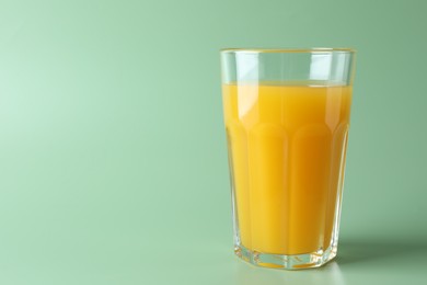 Photo of Tasty mango juice in glass on green background, space for text