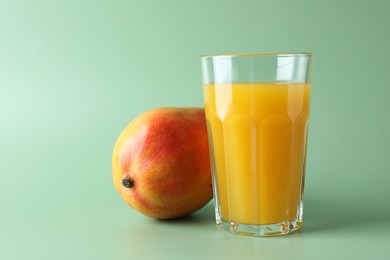 Photo of Tasty mango juice in glass and fresh fruit on green background
