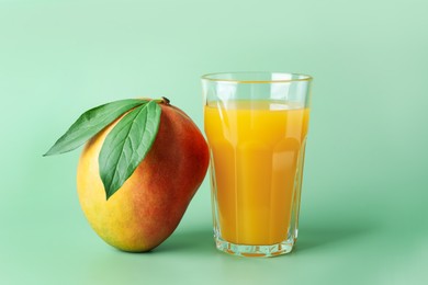 Photo of Tasty mango juice in glass and fresh fruit on green background