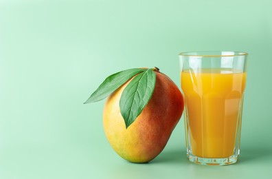 Photo of Tasty mango juice in glass and fresh fruit on green background, space for text