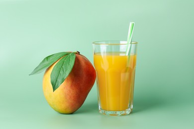 Photo of Tasty mango juice in glass and fresh fruit on green background