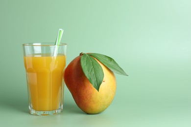 Photo of Tasty mango juice in glass and fresh fruit on green background, space for text