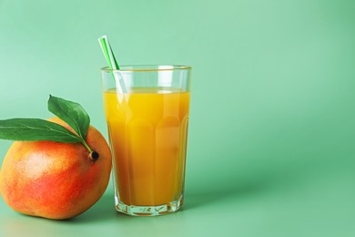 Photo of Tasty mango juice in glass and fresh fruit on green background, space for text