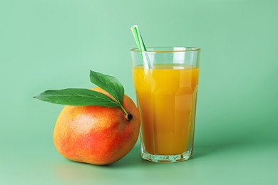 Photo of Tasty mango juice in glass and fresh fruit on green background
