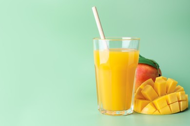 Photo of Tasty mango juice in glass and fresh fruits on green background, space for text
