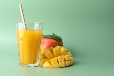 Photo of Tasty mango juice in glass and fresh fruits on green background, space for text
