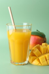 Photo of Tasty mango juice in glass and fresh fruits on green background, closeup
