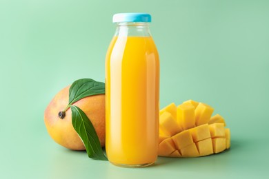 Photo of Tasty mango juice in glass bottle and fresh fruits on green background