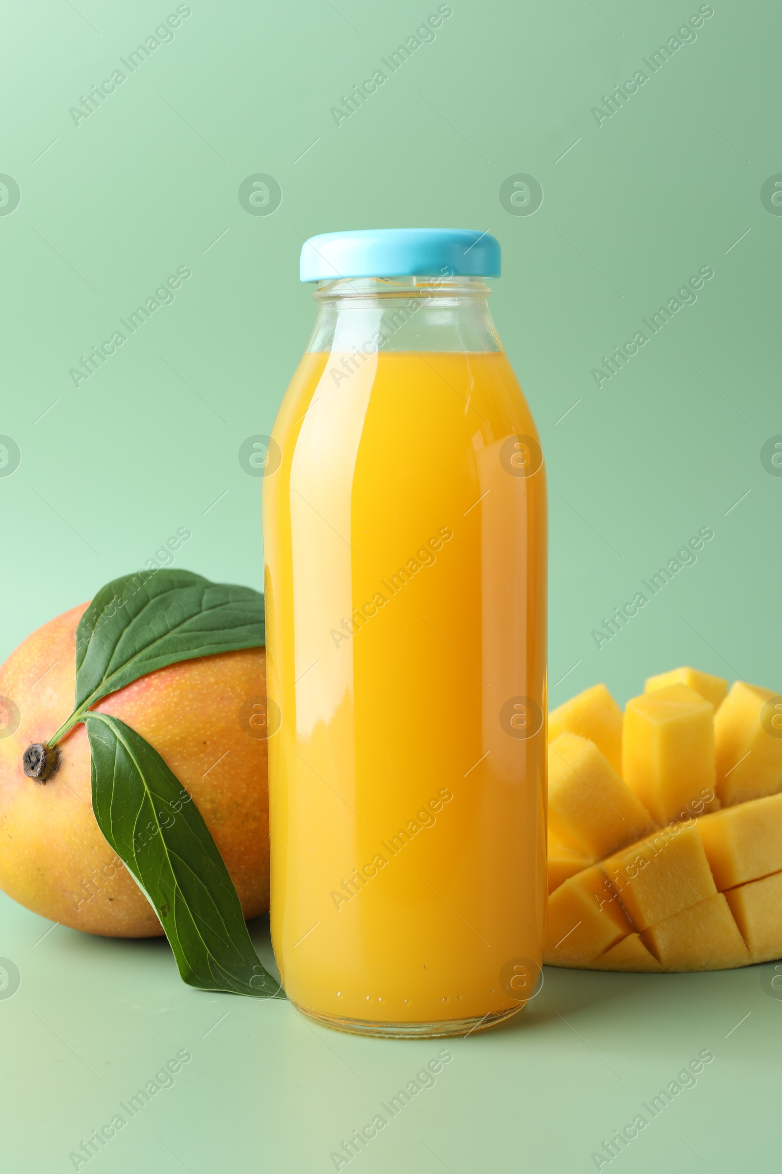 Tasty mango juice in glass bottle and fresh fruits on green background Photo of Tasty mango juice in glass bottle and fresh fruits on green background