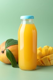 Photo of Tasty mango juice in glass bottle and fresh fruits on green background