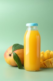 Photo of Tasty mango juice in glass bottle and fresh fruits on green background