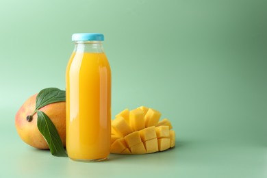 Photo of Tasty mango juice in glass bottle and fresh fruits on green background, space for text