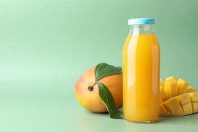 Photo of Tasty mango juice in glass bottle and fresh fruits on green background, space for text