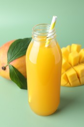 Photo of Tasty mango juice in glass bottle and fresh fruits on green background, closeup
