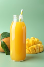 Photo of Tasty mango juice in glass bottle and fresh fruits on green background, closeup