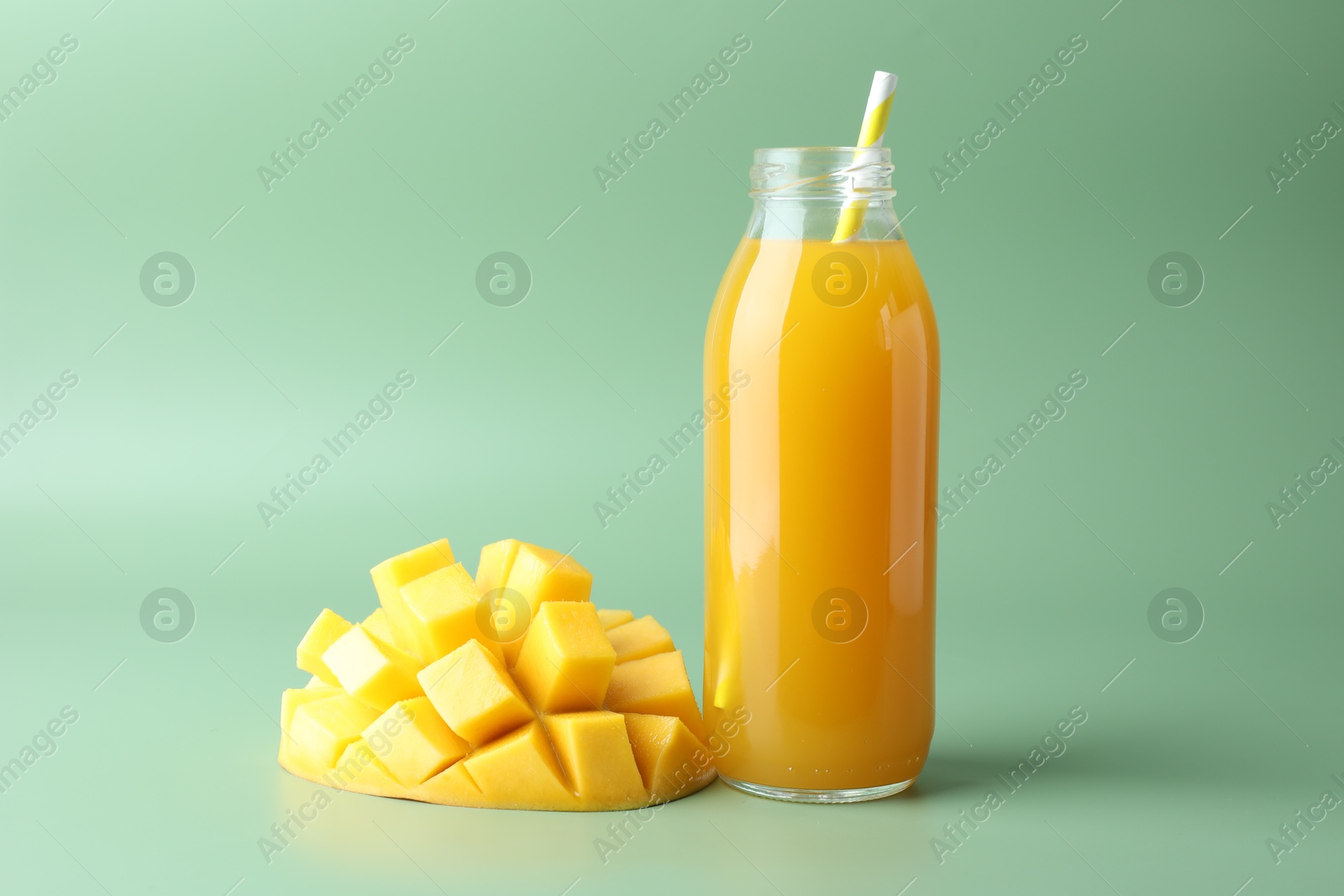 Tasty mango juice in glass bottle and fresh fruit on green background Photo of Tasty mango juice in glass bottle and fresh fruit on green background