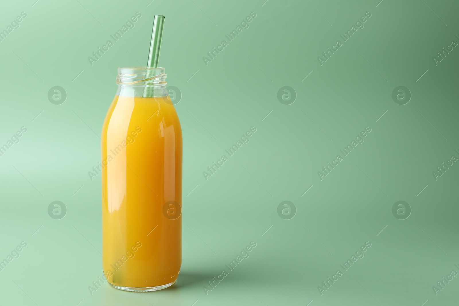 Tasty mango juice in glass bottle on green background, space for text Photo of Tasty mango juice in glass bottle on green background, space for text