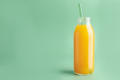 Photo of Tasty mango juice in glass bottle on green background, space for text