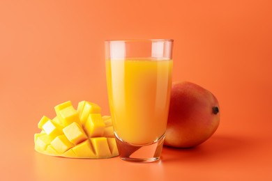 Photo of Tasty mango juice in glass and fresh fruits on orange background