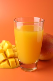 Photo of Tasty mango juice in glass and fresh fruits on orange background, closeup