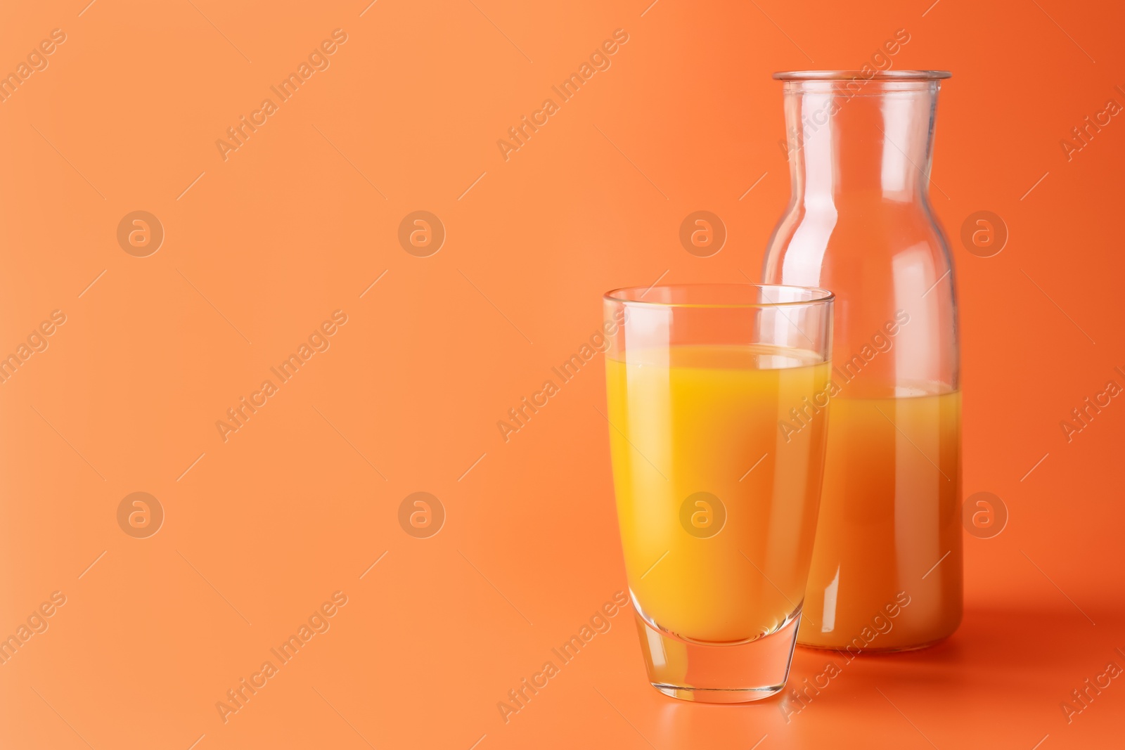 Tasty mango juice in glass and carafe on orange background, space for text Photo of Tasty mango juice in glass and carafe on orange background, space for text