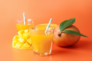 Photo of Tasty mango juice in glasses and fresh fruits on orange background