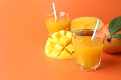 Photo of Tasty mango juice in glasses and fresh fruits on orange background, closeup. Space for text