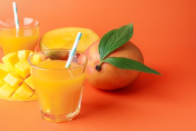 Photo of Tasty mango juice in glasses and fresh fruits on orange background, closeup. Space for text