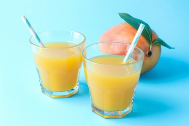 Photo of Tasty mango juice in glasses and fresh fruit on light blue background, closeup