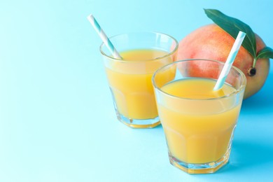 Photo of Tasty mango juice in glasses and fresh fruit on light blue background, closeup. Space for text