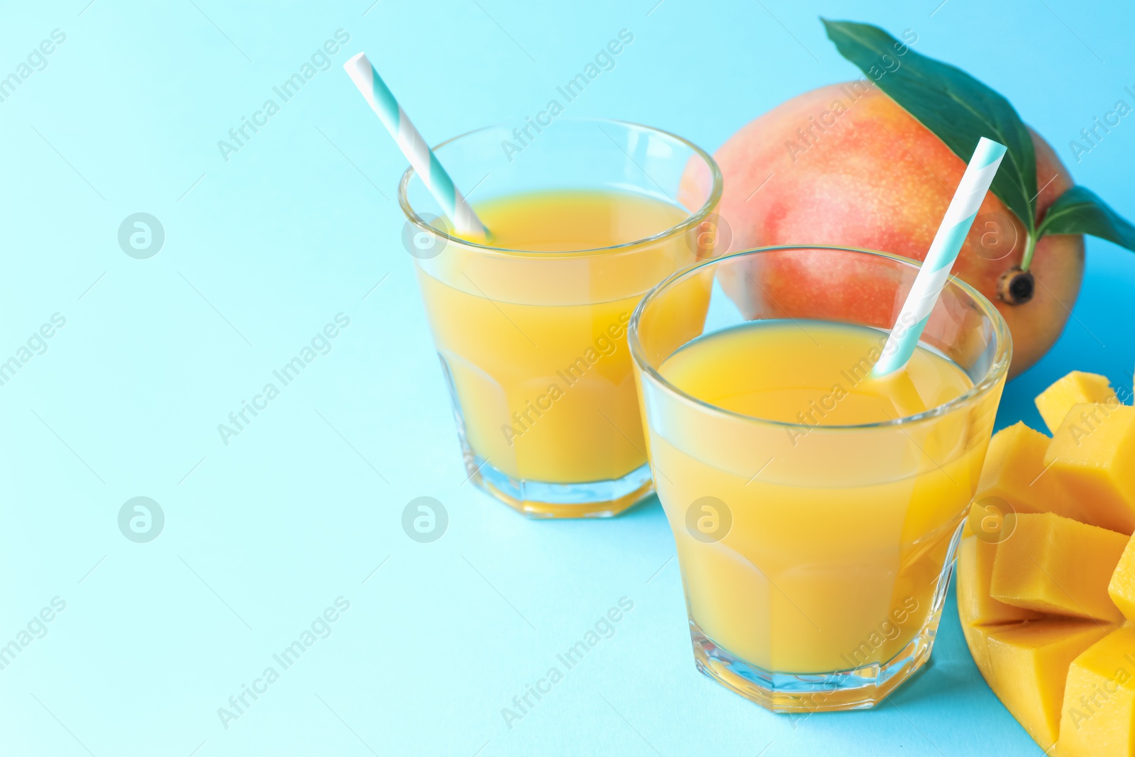 Tasty mango juice in glasses and fresh fruits on light blue background, closeup. Space for text Photo of Tasty mango juice in glasses and fresh fruits on light blue background, closeup. Space for text