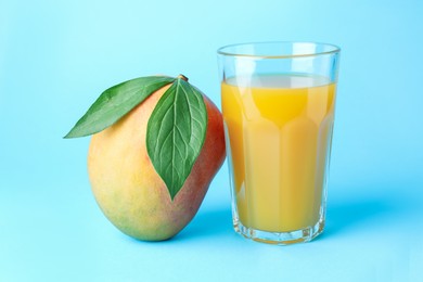 Photo of Tasty mango juice in glass and fresh fruit on light blue background