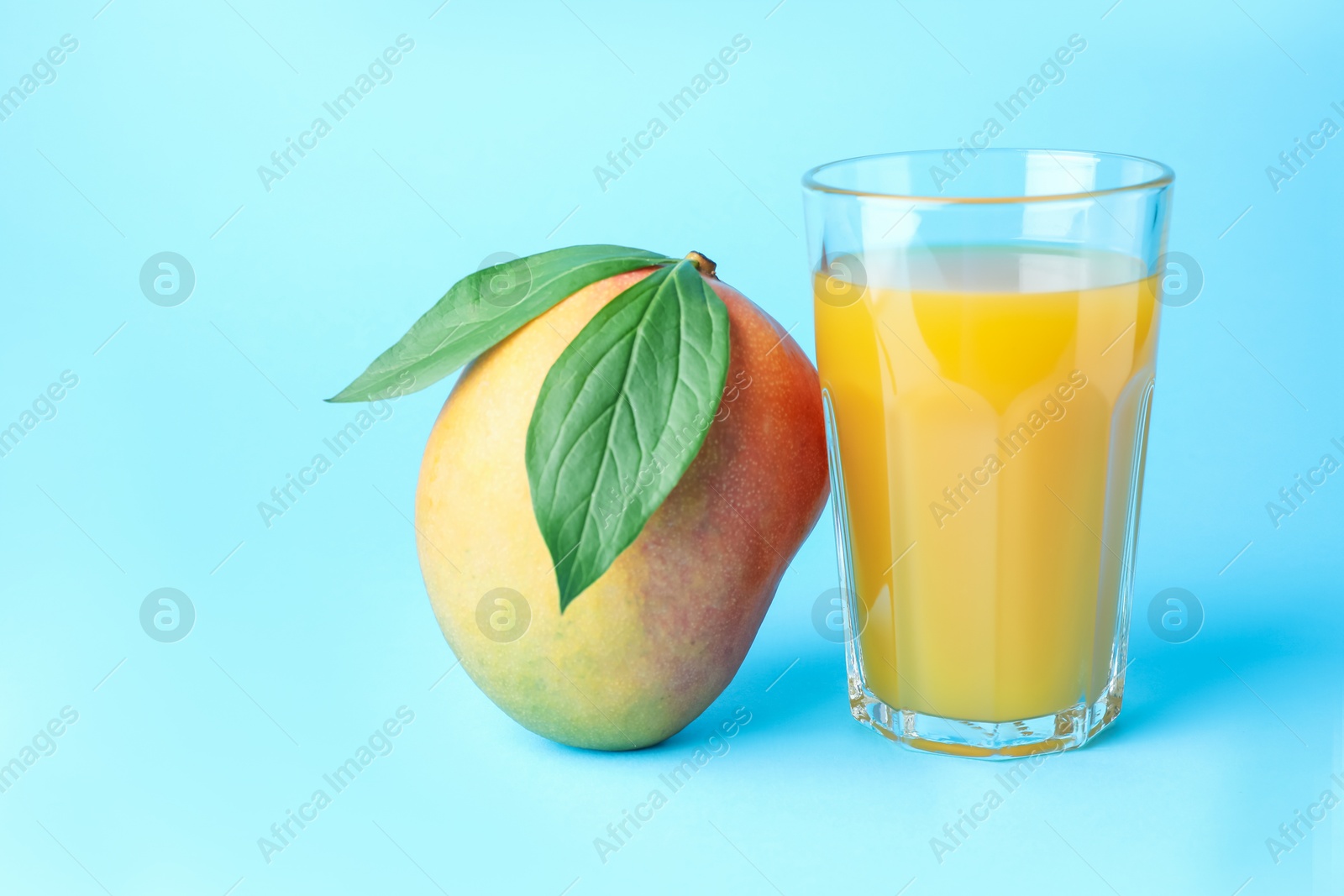 Tasty mango juice in glass and fresh fruit on light blue background Photo of Tasty mango juice in glass and fresh fruit on light blue background