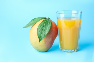 Photo of Tasty mango juice in glass and fresh fruit on light blue background