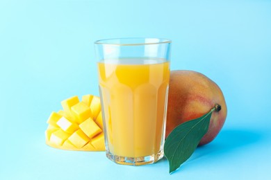 Photo of Tasty mango juice in glass and fresh fruits on light blue background, closeup