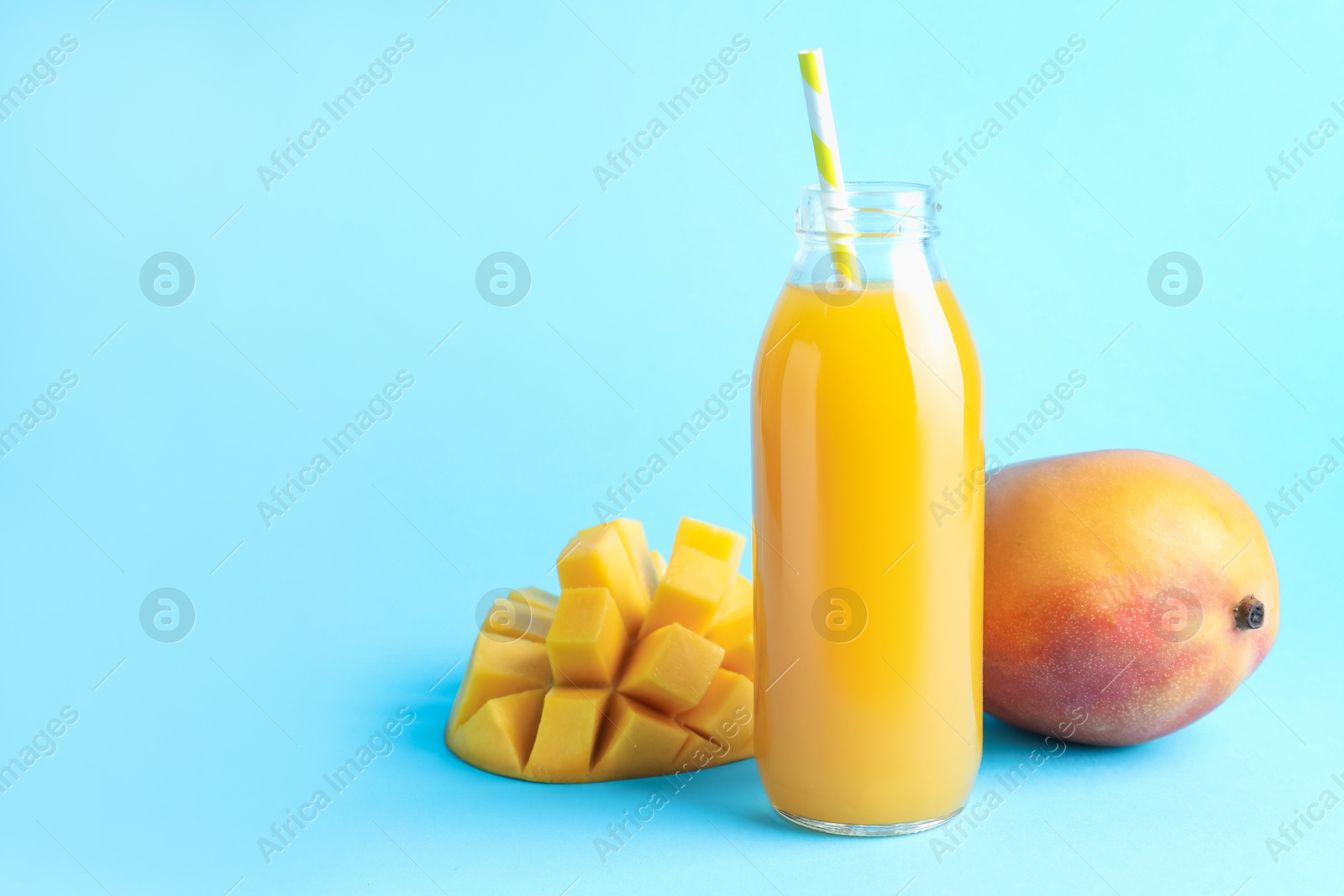 Tasty mango juice in glass bottle and fresh fruits on light blue background, space for text Photo of Tasty mango juice in glass bottle and fresh fruits on light blue background, space for text