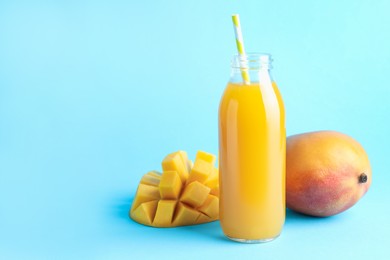 Photo of Tasty mango juice in glass bottle and fresh fruits on light blue background, space for text