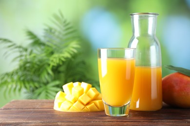 Photo of Tasty mango juice in glass, carafe and fresh fruits on wooden table against blurred background, space for text