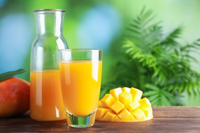 Photo of Tasty mango juice in glass, carafe and fresh fruits on wooden table against blurred background, space for text