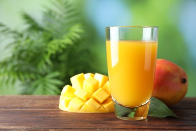 Photo of Tasty mango juice in glass and fresh fruits on wooden table against blurred background, space for text