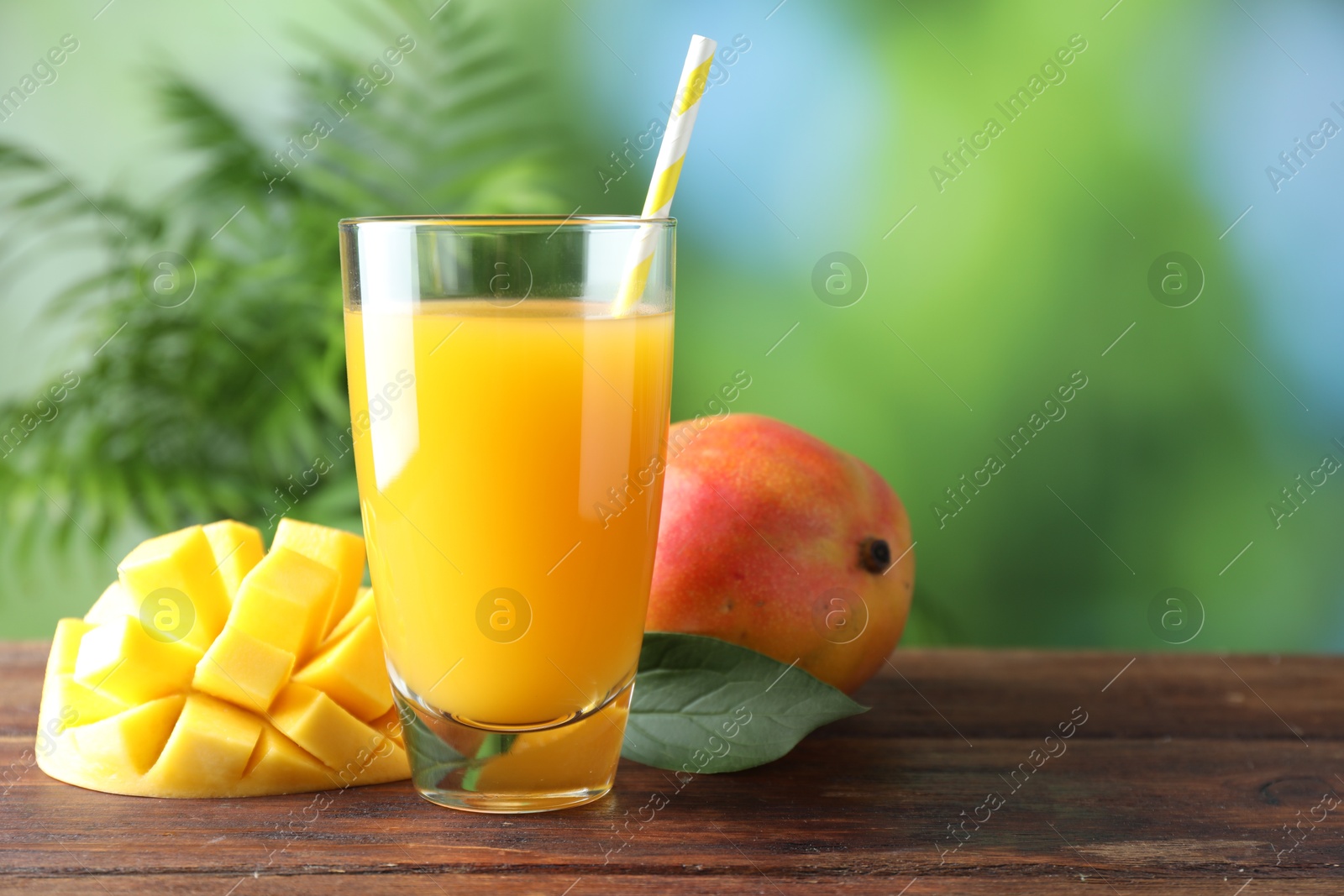 Tasty mango juice in glass and fresh fruits on wooden table against blurred background, space for text Photo of Tasty mango juice in glass and fresh fruits on wooden table against blurred background, space for text