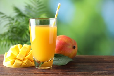 Photo of Tasty mango juice in glass and fresh fruits on wooden table against blurred background, space for text