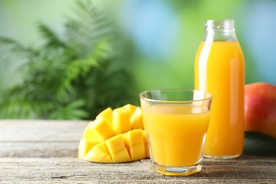 Photo of Tasty mango juice in glass, bottle and fresh fruits on wooden table against blurred background, closeup. Space for text