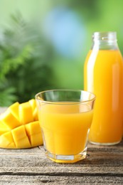 Photo of Tasty mango juice in glass, bottle and fresh fruit on wooden table against blurred background, closeup