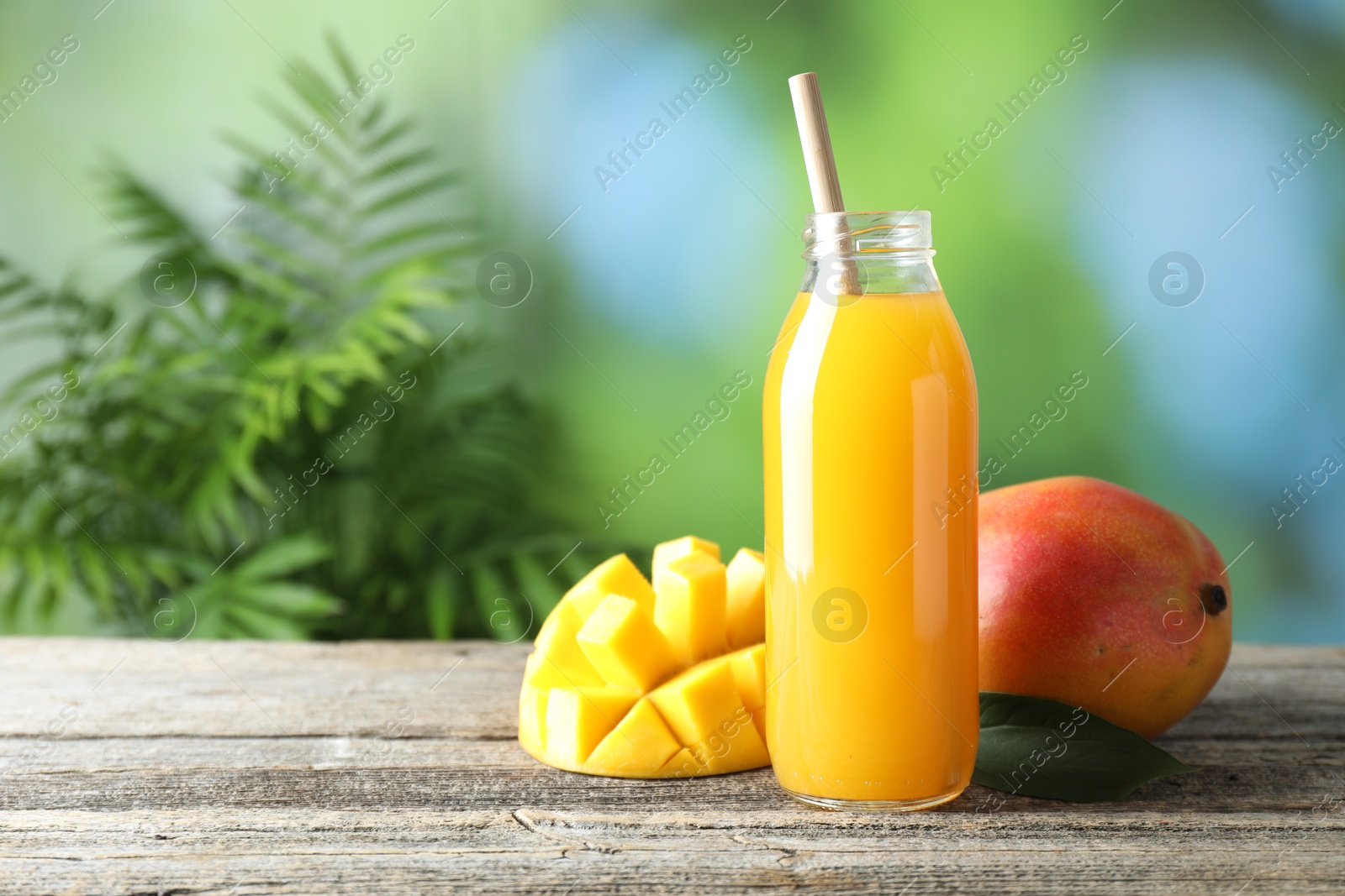 Tasty mango juice in glass bottle and fresh fruits on wooden table against blurred background, space for text Photo of Tasty mango juice in glass bottle and fresh fruits on wooden table against blurred background, space for text