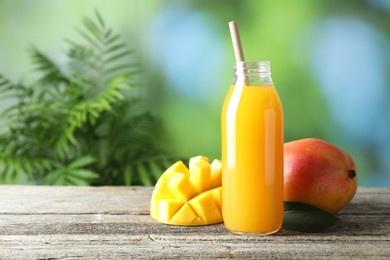 Photo of Tasty mango juice in glass bottle and fresh fruits on wooden table against blurred background, space for text