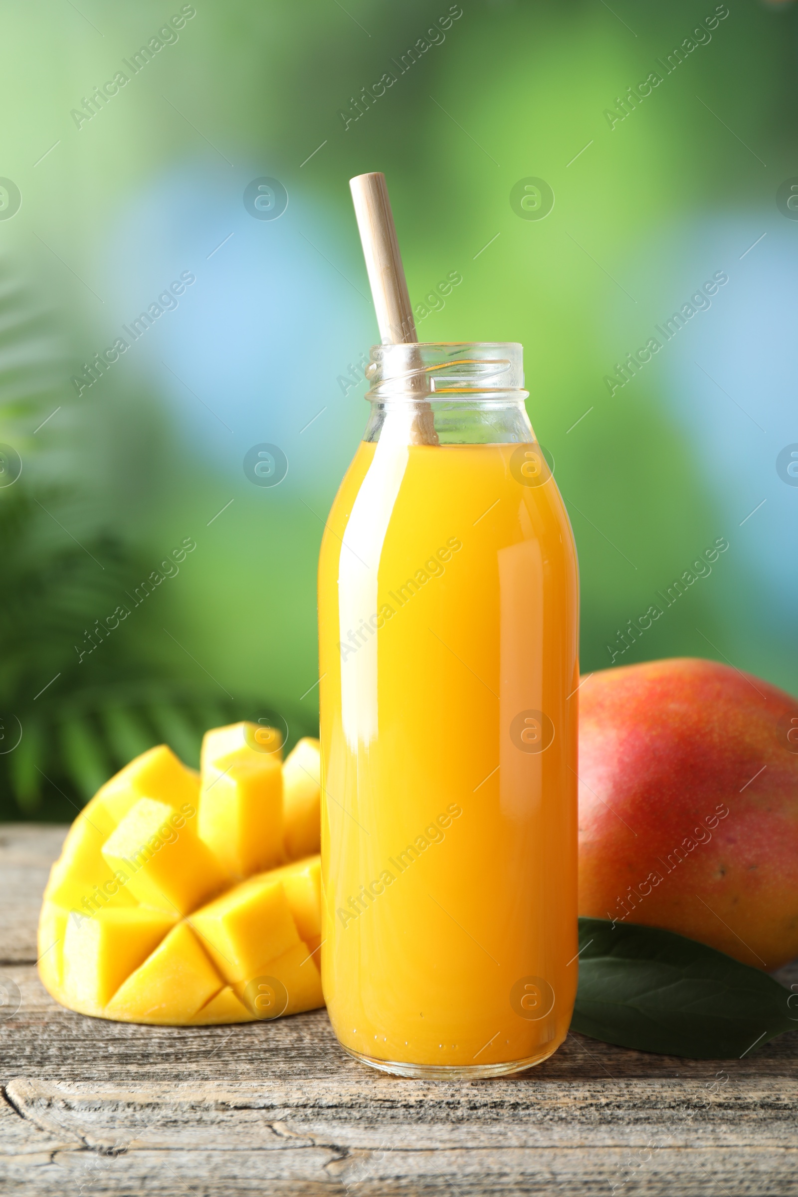 Tasty mango juice in glass bottle and fresh fruits on wooden table against blurred background Photo of Tasty mango juice in glass bottle and fresh fruits on wooden table against blurred background